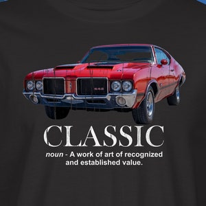 May include: A black t-shirt with a red classic car and the word "CLASSIC" in white text. The text below the car reads "noun - A work of art of recognized and established value."