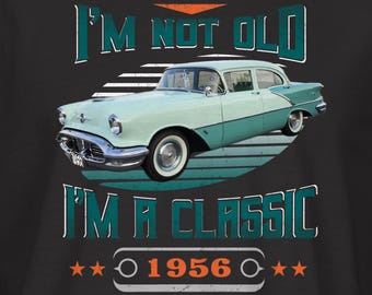 May include: Black t-shirt featuring a vintage car graphic in teal and white, with the text "I'M NOT OLD, I'M A CLASSIC" and the year "1956". The design includes stars and a circular border.