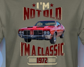 May include: A green t-shirt with a red 1972 Oldsmobile Cutlass. The shirt has the text "I'm Not Old I'm A Classic 1972" printed on it.