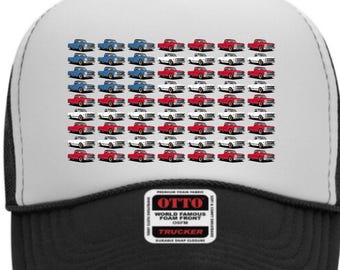 May include: Trucker hat with a white front panel featuring a pattern of red, white, and blue vintage pickup trucks. The hat has a black mesh back, a curved brim, and a snap closure. The hat has the text "OTTO WORLD FAMOUS FOAM FRONT OSFM TRUCKER" on the front.