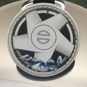 May include: A white and black car wheel keychain with a silver rim and the word "HYDRA" printed in blue and green letters.