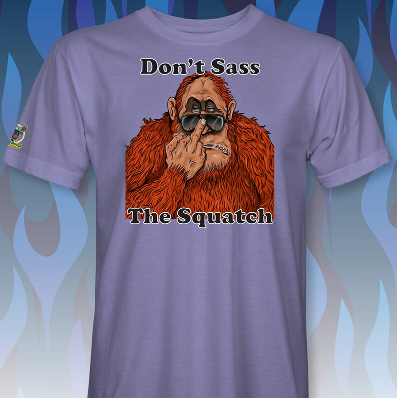 Peut inclure: T-shirt violet avec une image de dessin anim&eacute; d'un sasquatch portant des lunettes de soleil et faisant un doigt d'honneur. Le texte "Don't Sass The Squatch" est imprim&eacute; sur le t-shirt.