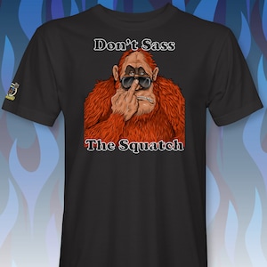 Peut inclure: T-shirt noir avec un graphique d'un sasquatch portant des lunettes de soleil et faisant un doigt d'honneur. Le texte "Don't Sass The Squatch" est imprim&eacute; sous l'image.