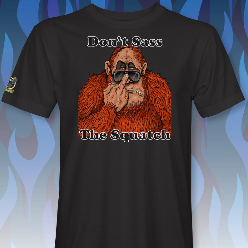 Peut inclure: T-shirt noir avec un graphique d'un sasquatch portant des lunettes de soleil et faisant un doigt d'honneur. Le texte "Don't Sass The Squatch" est imprim&eacute; sous l'image.
