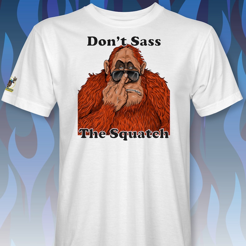 Peut inclure: T-shirt blanc avec une image de dessin anim&eacute; d'un sasquatch portant des lunettes de soleil et faisant un doigt d'honneur. Le texte "Don't Sass The Squatch" est imprim&eacute; sous l'image.