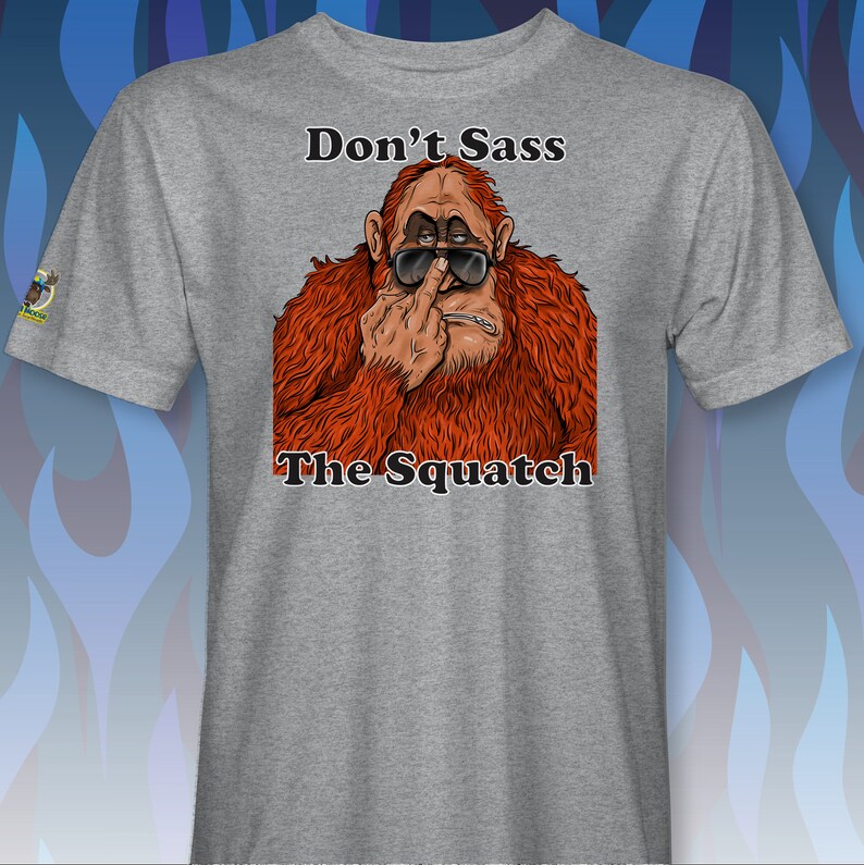 Peut inclure: Un t-shirt gris avec un graphique d'un sasquatch portant des lunettes de soleil et faisant un doigt d'honneur. Le texte "Don't Sass The Squatch" est imprim&eacute; sous l'image.