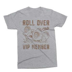 May include: A heather gray t-shirt with a brown graphic of a vehicle flipped over. The text "ROLL OVER Club VIP MEMBER" is printed above and below the vehicle illustration.