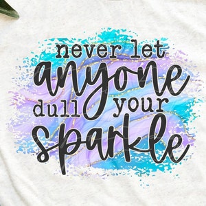 Op de afbeelding: Een wit T-shirt met een blauw, paars en gouden marmerdessin. De tekst "never let anyone dull your sparkle" staat in zwart op het marmerdessin.