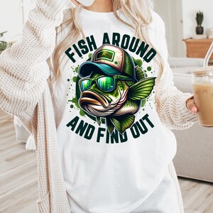 May include: White t-shirt with a green, blue, and black cartoon fish wearing sunglasses and a hat. The text "Fish Around and Find Out" is printed on the shirt.