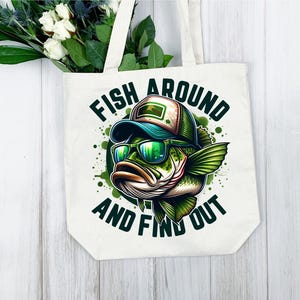 May include: White canvas tote bag with a green, black, and blue illustration of a bass fish wearing sunglasses and a hat. The text "Fish Around And Find Out" is printed on the bag.