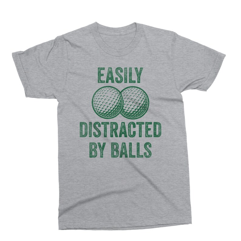 Puede incluir: Camiseta gris jaspeado con el texto verde "EASILY DISTRACTED BY BALLS". El dise&ntilde;o incluye dos pelotas de golf verdes. Cuello redondo y mangas cortas.