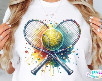 May include: A white t-shirt with a colorful design of two tennis rackets crossed over a sparkling yellow tennis ball. The design is surrounded by colorful dots and splatters.