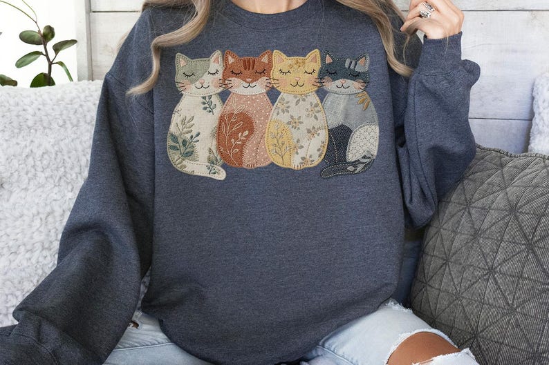 Pu&ograve; includere: Felpa grigio scuro con un design applicato di quattro gatti stilizzati. Ogni gatto ha un motivo e un colore unici, tra cui beige con foglie verdi, marrone con accenti arancioni, giallo con dettagli floreali e grigio con una coda nera.