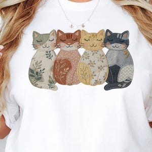 Pu&ograve; includere: T-shirt bianca con quattro applicazioni di gatti. Ogni gatto ha un motivo e un colore unici, tra cui verde, marrone, giallo e grigio. I gatti sono disposti in fila, con gli occhi chiusi, dando un aspetto stravagante. La maglietta &egrave; un capo casual per tutti i giorni.