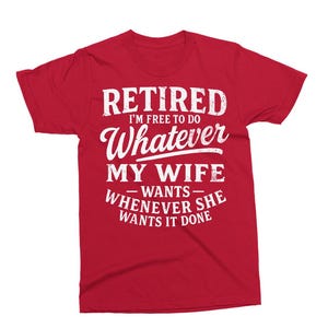 May include: Red t-shirt with white text: "RETIRED I'M FREE TO DO Whatever MY WIFE wants WHENEVER SHE WANTS IT DONE". The tee has short sleeves and a crew neck.