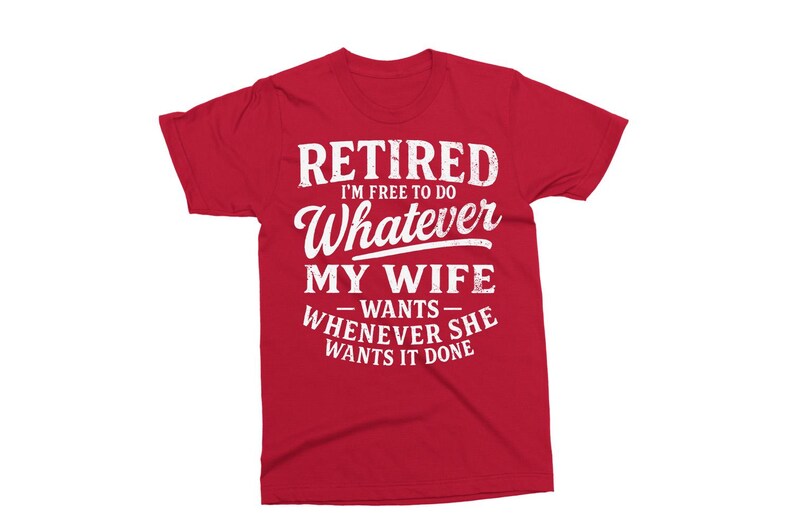 May include: Red t-shirt with white text: "RETIRED I'M FREE TO DO Whatever MY WIFE wants WHENEVER SHE WANTS IT DONE". The tee has short sleeves and a crew neck.