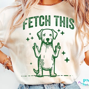 May include: A white t-shirt with a green graphic of a dog giving the middle finger with the text "FETCH THIS" above the dog.