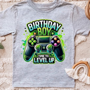 May include: Gray t-shirt with a green, blue, and black video game controller graphic. The text "Birthday Boy" and "Time to Level Up" is printed on the shirt.