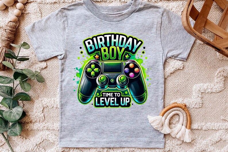 May include: Gray t-shirt with a green, blue, and black video game controller graphic. The text "Birthday Boy" and "Time to Level Up" is printed on the shirt.