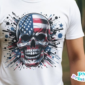 May include: A white t-shirt with a graphic of a skull with an American flag design. The skull is surrounded by black paint splatters.