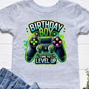 May include: Gray t-shirt with a green and black video game controller graphic. The text "Birthday Boy" and "Time to Level Up" is printed on the shirt.