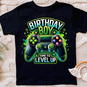 May include: Black t-shirt with a green, blue, and black video game controller graphic. The text "Birthday Boy" and "Time to Level Up" is printed on the shirt.