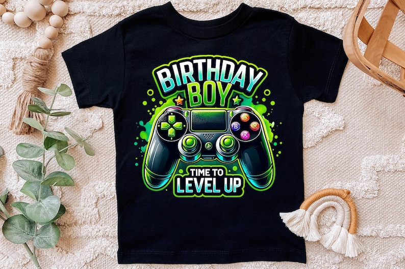 May include: Black t-shirt with a green, blue, and black video game controller graphic. The text "Birthday Boy" and "Time to Level Up" is printed on the shirt.