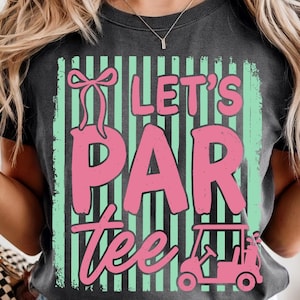 May include: Dark grey t-shirt with a pink and green graphic that says "Let's Par Tee". The design includes a golf cart and a bow. The shirt is a casual style.