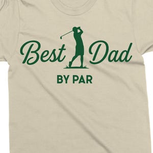 K&ouml;nnte beinhalten: Beiges T-Shirt mit dem gr&uuml;nen Schriftzug "Best Dad" und einer gr&uuml;nen Silhouette eines Golfspielers. Darunter steht "BY PAR". Ein ideales Geschenk f&uuml;r Golf-Fans.