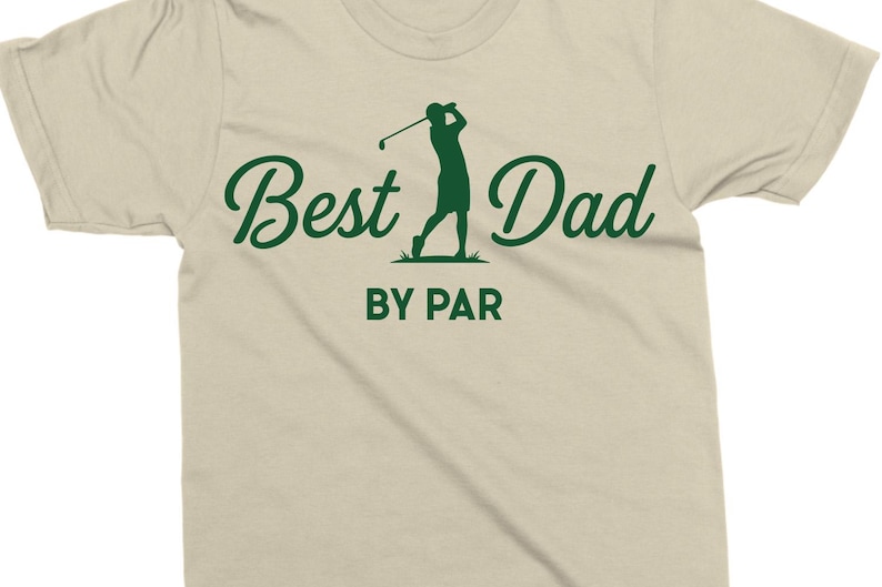 K&ouml;nnte beinhalten: Beiges T-Shirt mit dem gr&uuml;nen Schriftzug "Best Dad" und einer gr&uuml;nen Silhouette eines Golfspielers. Darunter steht "BY PAR". Ein ideales Geschenk f&uuml;r Golf-Fans.