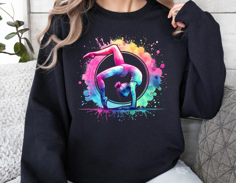 May include: Black sweatshirt with a colorful watercolor design of a gymnast performing a handstand on a ring. The design features splashes of pink, blue, green, and yellow.