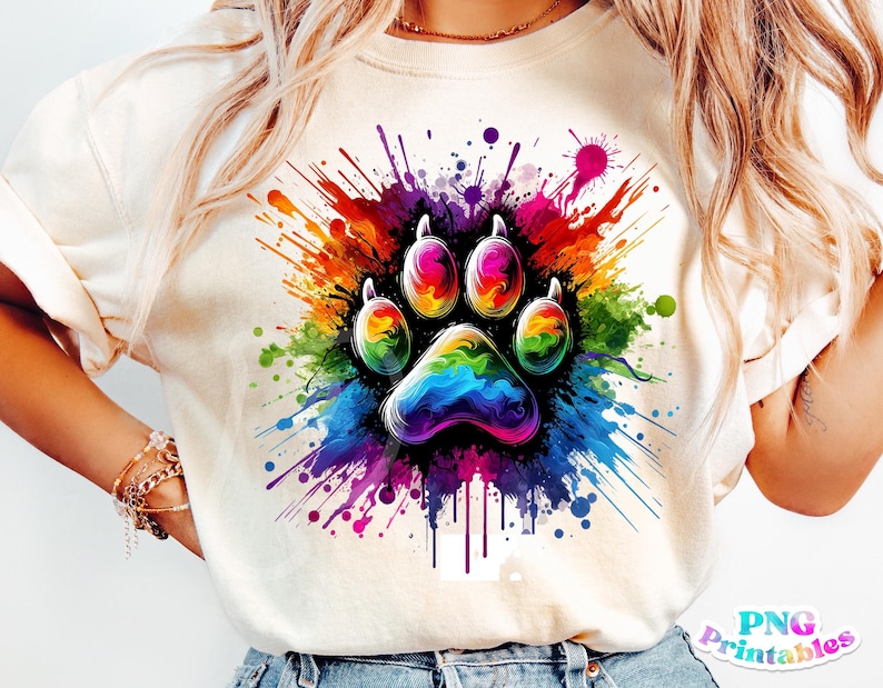 Może przedstawiać: Biała koszulka z kolorowym wzorem odcisku łapy. Odcisk łapy jest otoczony kolorowymi plamami farby w kolorze tęczy.