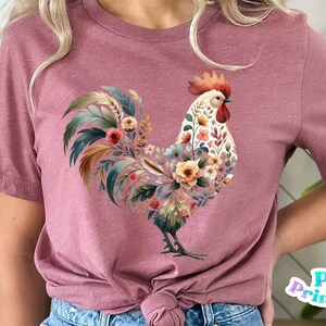 May include: A pink t-shirt with a floral rooster design. The rooster is made up of flowers and leaves in shades of pink, yellow, green, and brown.