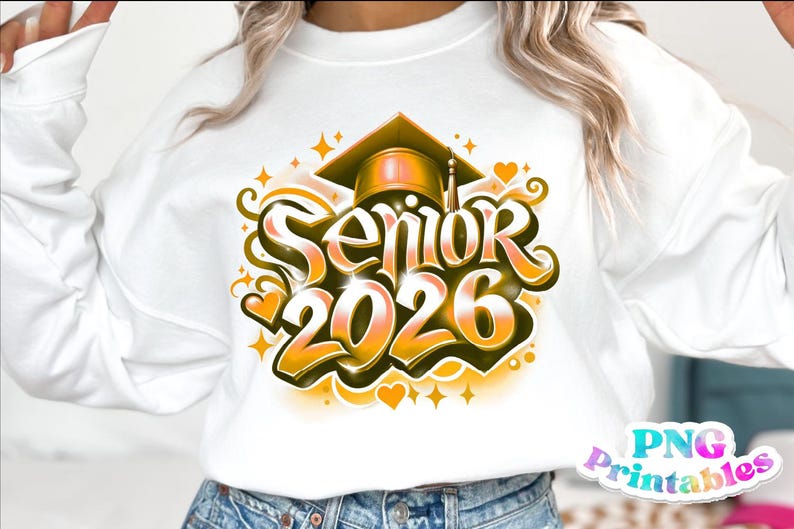 K&ouml;nnte beinhalten: Wei&szlig;es Sweatshirt mit einem Abschluss-Design. Das Design zeigt den Text "Senior 2026" in einer stilisierten Schriftart, eine Abschlusskappe, Sterne und Herzen in Gold- und Oranget&ouml;nen. Das Sweatshirt ist ein l&auml;ssiges Kleidungsst&uuml;ck.