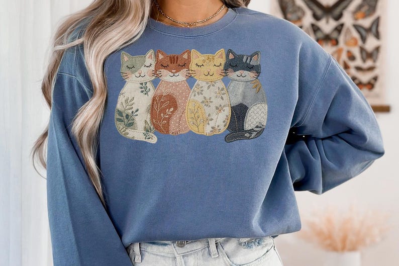 Pu&ograve; includere: Una felpa blu con un ricamo di quattro gatti stilizzati. Ogni gatto ha un motivo unico, tra cui disegni floreali e patchwork, nelle tonalit&agrave; del verde, marrone, giallo e grigio. La felpa &egrave; di colore blu unito.