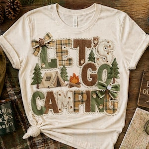 May include: Cream-colored t-shirt with the phrase "LET'S GO CAMPING" in patchwork letters, featuring camping-themed appliqués. The image includes a lantern, mug, backpack, and a wooden sign that says "LIFE IS BETTER OUTDOORS".