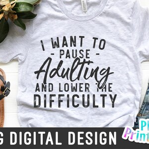 May include: A white t-shirt with a black graphic that says "I want to - pause - Adulting and lower the difficulty".