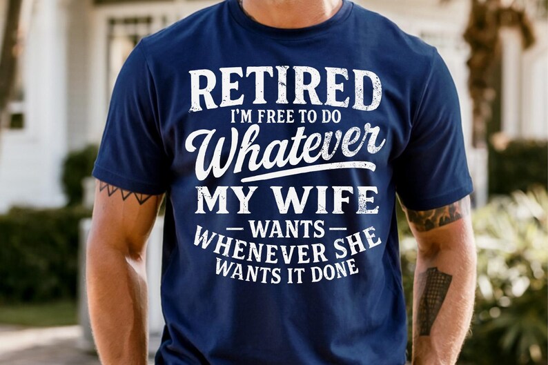 May include: Navy blue t-shirt with white text that reads "RETIRED I'M FREE TO DO Whatever MY WIFE WANTS WHENEVER SHE WANTS IT DONE". The shirt is a crew neck and has short sleeves.