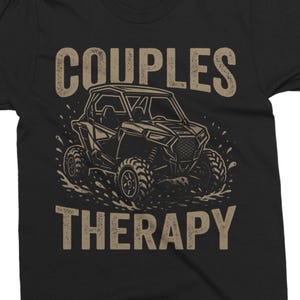 May include: Black t-shirt with a graphic of an off-road vehicle in a water splash. The words "COUPLES" and "THERAPY" are printed above and below the vehicle in a distressed, tan font. The design is centered on the shirt.