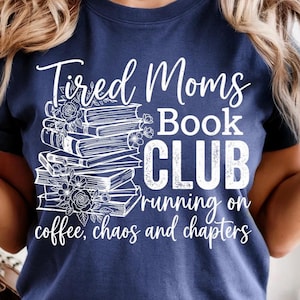 Peut inclure: T-shirt bleu marine avec texte blanc et motif sur le thème des livres. Le texte dit "Tired Moms Book Club" avec une pile de livres et des accents floraux. Le texte supplémentaire dit "running on coffee, chaos and chapters."