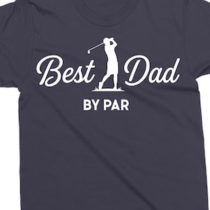 K&ouml;nnte beinhalten: Dunkelblaues T-Shirt mit dem Schriftzug "Best Dad" in Schreibschrift, begleitet von einer Silhouette eines Golfspielers. Der Satz "BY PAR" ist darunter in einer serifenlosen Schriftart gedruckt. Golf-Thema.