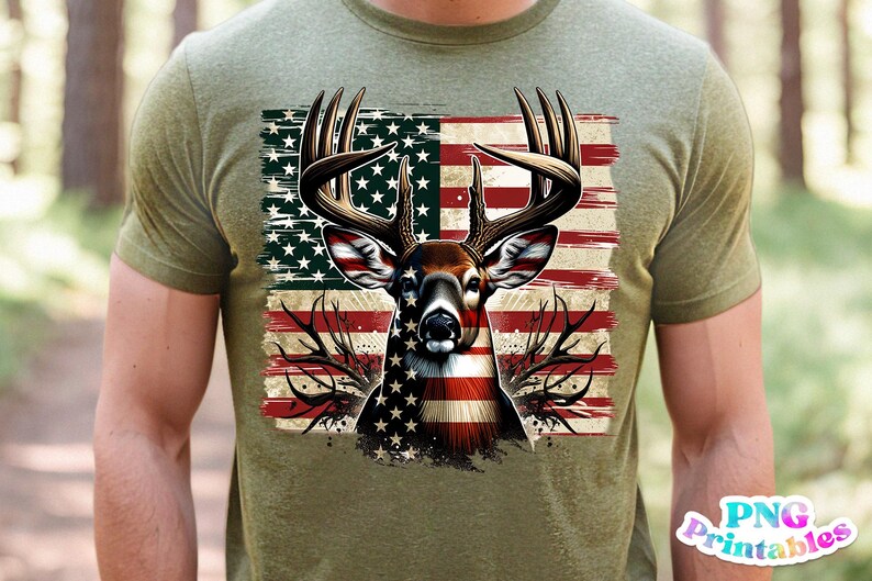 May include: Olive green t-shirt featuring a deer head design with antlers, superimposed over an American flag. The deer's face is detailed with the flag's stars and stripes. The shirt is a casual wear item.