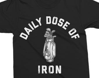 May include: Black t-shirt with a distressed white graphic. The graphic features a golf bag with clubs and the text "DAILY DOSE OF IRON" in a curved font above the bag and straight text below. The shirt is made of a soft material.
