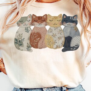 Pu&ograve; includere: Felpa color crema con un disegno di quattro gatti stilizzati. Ogni gatto ha un motivo e un colore unici, tra cui verde, marrone, giallo e blu. I gatti sono disposti in fila, con gli occhi chiusi, creando un'estetica stravagante e artistica.