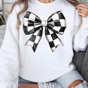 May include: White sweatshirt with a black and white checkered bow design.