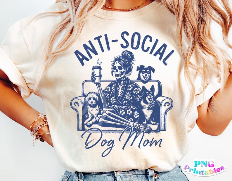 Może przedstawiać: Biały T-shirt z niebieskim nadrukiem graficznym, na kt&oacute;rym widnieje napis "Anti-Social Dog Mom". Grafika przedstawia szkielet trzymający kubek kawy i siedzący na kanapie z trzema psami.