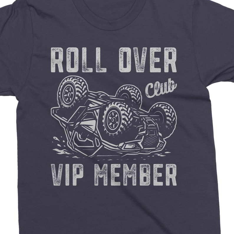 May include: Dark navy blue t-shirt with a distressed graphic. The graphic features a vehicle flipped over with the text "ROLL OVER Club VIP MEMBER" in a vintage font. The design is in shades of gray and white.