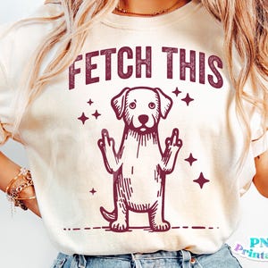 May include: A white t-shirt with a maroon graphic of a dog giving the middle finger with the text "FETCH THIS" above the dog.