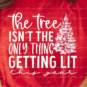 以下が含まれることがあります： 赤いTシャツに、「The tree isn't the only thing getting lit this year」という白い文字が書かれています。テキストの右側に、白いスタイリッシュなクリスマスツリーがあります。