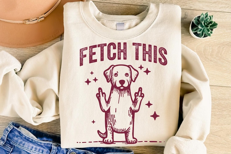 May include: A cream-colored sweatshirt with a maroon graphic of a dog giving the middle finger with the text "FETCH THIS" above it.